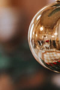 Nahaufnahme eines glänzenden goldenen Ornaments, das eine verschwommene Innenszene widerspiegelt, perfekt, um die Stimmung für eine intime Hochzeit zu schaffen. Der Hintergrund zeichnet sich durch warme Töne und sanftes Licht aus und schafft eine festliche und gemütliche Atmosphäre, ideal für eine elegante Hochzeitsplanung.