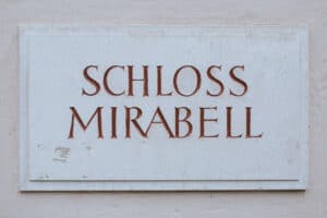 Eine Steintafel mit den in Großbuchstaben eingravierten Worten „Schloss Mirabell“ ziert eine helle Wand und weckt Träume von eleganten Hochzeiten und fachmännischer Hochzeitsplanung.