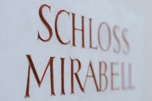 Nahaufnahme eines eingravierten Schildes mit den Worten „Schloss Mirabell“ in roten Großbuchstaben auf einer hellen Steinoberfläche, einem für Hochzeitsfeiern berühmten Ort.