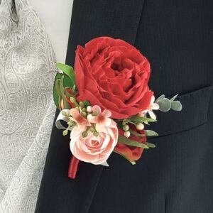 Nahaufnahme eines schwarzen Anzugs mit einer leuchtend roten Rose als Ansteckblume, perfekt für eine Hochzeit oder einen anderen besonderen Anlass. Es zeigt eine hellrosa Rose und kleine weiße Blumen, ergänzt durch eine silber gemusterte Krawatte und eine passende Weste darunter, ideal für alle, die sich auf Hochzeitsplanung konzentrieren.