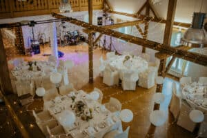 Ein wunderschön dekorierter Ort für Ihre Hochzeit, perfekt für Ihre Hochzeit, mit runden Tischen mit weißen Tischdecken und Blumendekorationen. Sanft leuchtende Lichterketten und Papierlaternen hängen darüber und schaffen eine warme und einladende Atmosphäre, ideal für Ihre Hochzeitsfeier.