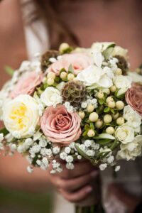 Ein perfekter Hochzeitsstrauß mit rosa, weißen und gelben Rosen, Akzenten aus Schleierkraut, grünen Blättern und kleinen beigen Beeren. Ideal für Ihre Hochzeitsplanung.