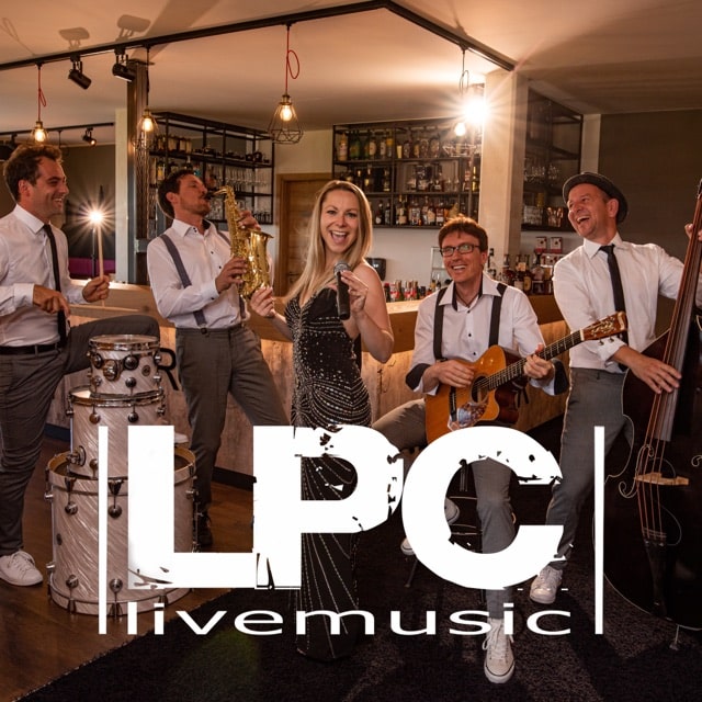Eine Band tritt drinnen auf, mit einem Sänger in der Mitte, umgeben von Musikern, die Saxophon, Gitarre, Kontrabass und Schlagzeug spielen. In formeller Kleidung vor einer Bar im Hintergrund verleihen sie jeder Hochzeit eine elegante Note. Auf dem Bild steht „LPC Live-Musik“.