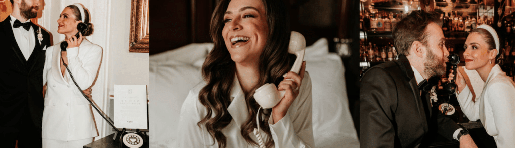 Eine Frau in weißem Outfit lächelt, während sie ein altes Telefon mit Wählscheibe benutzt und vielleicht über die Hochzeitsplanung spricht. Sie wird von einem Mann in Abendgarderobe begleitet. Die Umgebung ist elegant und gemütlich zugleich, mit dunklem Holz und stimmungsvollem Licht, perfekt, um ihre Liebe und Verbundenheit zu feiern.