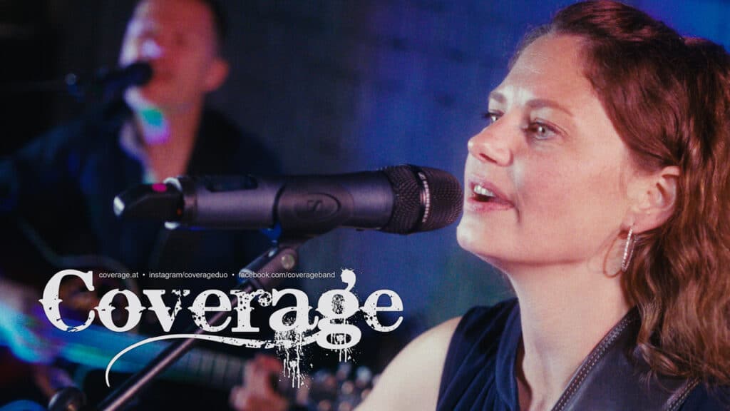 Eine Frau singt in ein Mikrofon, ihre Augen sind offen und konzentriert. Im Hintergrund spielt eine verschwommene Figur Gitarre. Das Wort „Coverage“ wird stilvoll über das Bild gelegt. Die Beleuchtung ist eine Mischung aus blauen und violetten Farbtönen.