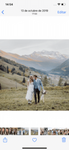 Ein Paar im Hochzeitskleid steht eng beieinander auf einem grasbewachsenen Hügel und genießt den bezaubernden Reiz seiner Hochzeit. Schneebedeckte Gipfel und immergrüne Bäume schmücken die Berglandschaft und schaffen eine ruhige und malerische Kulisse für diesen unvergesslichen Moment.