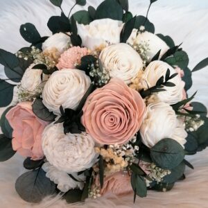 Ein Strauß mit zartrosa und cremefarbenen Rosen, akzentuiert mit Grün und kleinen weißen Füllblumen, elegant arrangiert auf einem weißen strukturierten Hintergrund – perfekt für eine Hochzeitsfeier.