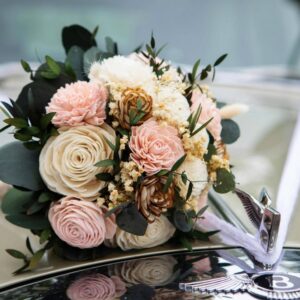 Ein Strauß zartrosa, cremefarbener und weißer Rosen mit grünem Blattwerk ziert elegant die Motorhaube eines Oldtimers. Das „B“-Emblem glitzert im Vordergrund und schafft eine zeitlose Szene, die sich perfekt für jede Hochzeit oder Hochzeitsplanung eignet.