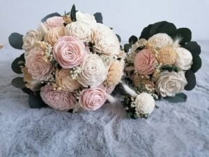 Zwei elegante Sträuße aus zartrosa und cremefarbenen Rosen mit Grün, arrangiert auf einer plüschig-grauen Oberfläche, perfekt für die Hochzeitsplanung. Die Blüten sind mit Schleierkraut vermischt und sorgen für ein zartes und romantisches Erscheinungsbild, ideal für Ihren besonderen Tag.