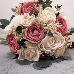 Ein Strauß mit weißen und staubrosa Rosen, akzentuiert mit kleinen weißen Blüten und grünen Blättern, arrangiert auf einer weichen grauen Oberfläche. Mit seinem natürlichen, eleganten Aussehen ist er perfekt für die Hochzeitsdekoration oder Hochzeitsplanung und sorgt dafür, dass sich jeder besondere Anlass wirklich exquisit anfühlt.