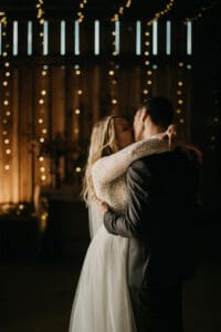 Braut und Bräutigam küssen sich romantisch in einem schwach beleuchteten, mit Lichterketten geschmückten Raum. Die Braut trägt ein Spitzenkleid, während der Bräutigam einen Anzug trägt. Das warme Leuchten der Lichter schafft eine intime, magische Atmosphäre – perfekt für ihre Hochzeitsfeier.