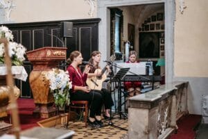 Drei Frauen spielen in einer Kirche bezaubernde Musik und schaffen so die ideale Atmosphäre für eine Hochzeit. Eine spielt Geige, eine andere Gitarre und die dritte Klavier, alles umgeben von Blumenarrangements und kunstvollem Dekor, die diesem besonderen Tag der Hochzeit noch mehr Schönheit verleihen.