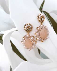 Elegante Tropfenohrringe mit pfirsichfarbenen Steinen, perfekt für eine Hochzeit, geschmückt mit kleinen Perlen und Strasssteinen, die sich vor weichen weißen Blütenblättern abheben.