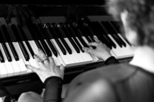 Auf einem Schwarzweißbild spielt eine Person auf einem Klavier, auf dem „Johannes Seiler“ eingraviert ist, und ihre Hände tanzen energisch über die Tasten. Der Fokus liegt auf ihrem harmonischen Zusammenspiel, das an die Eleganz erinnert, die man bei der Hochzeitsplanung sucht.