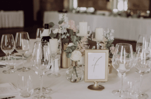 Ein Hochzeitstisch mit der Tischnummer „7“ in einem goldenen Rahmen. Umgeben von Weingläsern, Blumenarrangements und Kerzen entsteht eine elegante und romantische Atmosphäre – perfekt für jede Hochzeitsfeier.