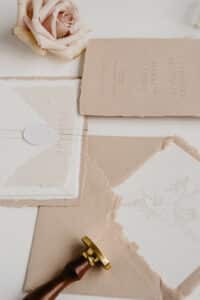 Elegante Hochzeitspapeterie mit beige- und rosafarbenen Einladungen mit zarter Schrift und Blumenillustrationen gibt den perfekten Ton für Ihre Hochzeit an. Eine Rose, ein Wachsstempel und Umschläge vervollständigen diese raffinierte, romantische Atmosphäre.