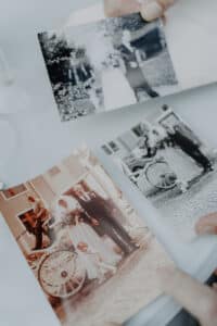 Hände halten und betrachten vorsichtig alte Hochzeitsfotos von Braut und Bräutigam, die neben einer Kutsche stehen. Die schwarz-weißen, sepiafarbenen Bilder wecken Nostalgie und verleihen jeder Hochzeit zeitlosen Charme. Die perfekte Inspiration für alle, die gerade mitten in den Hochzeitsvorbereitungen stecken.