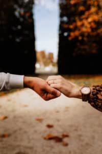 Zwei Menschen in lässigen Langarmshirts stoßen draußen mit den Fäusten aneinander, vor dem verschwommenen Hintergrund von Herbstlaub. An einem Handgelenk trägt man eine Uhr, was Einheit und Verbundenheit symbolisiert – ähnlich der Harmonie, die Paare bei der Hochzeitsplanung suchen.