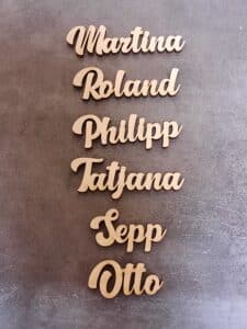 Die ausgeschnittenen Namen „Martina“, „Roland“, „Philipp“, „Tatjana“, „Sepp“ und „Otto“ sind vertikal auf grauem Hintergrund angeordnet und verleihen Ihrer Hochzeitsplanung eine charmante Note.