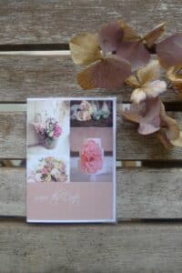 Eine Save-the-Date-Karte auf Holzoberfläche mit Blumenbildern und rosa Akzenten, perfekt für Ihre Hochzeitsplanung. Getrocknete Blumen werden daneben platziert und verleihen Ihrer schönen Einladung zur Hochzeit einen Hauch rustikaler Romantik.