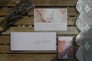 Eine Hochzeitseinladung auf einem Holztisch mit Spitzendeckchen und Lavendelzweig fängt die Essenz der Hochzeitsplanung ein. Die Einladung zeigt ein Foto einer Braut mit einem Blumenstrauß, elegante Typografie und die Namen „Michael & Marie“.