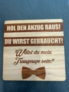 Auf einer Holztafel mit deutschem Text steht: „Hol den Anzug raus! Du wirst gebraucht! Willst du mein Trauzeuge sein?“ Perfekt, um Ihrer Hochzeitsplanung eine besondere Note zu verleihen, verfügt es über eine Fliege-Grafik am unteren Rand.