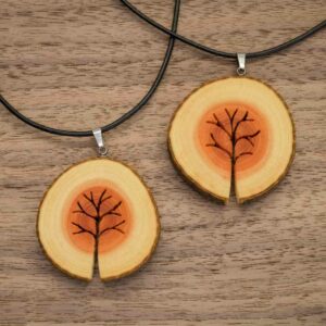Zwei Halsketten mit Anhängern aus Holzscheiben liegen auf einer Holzoberfläche. Perfekt für eine Hochzeit, jeder Anhänger weist ein geschnitztes Baumdesign auf, das die natürlichen Ringe und Farben des Holzes hervorhebt.