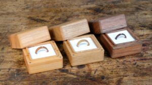Ringschachteln aus Holz werden auf einer Holzoberfläche präsentiert und eignen sich perfekt für jede Hochzeit. Jede Schachtel hat einen aufgeklappten Deckel, der den Blick auf den Ring im Inneren freigibt. Die Schachteln haben unterschiedliche Holztöne und ihr schlichtes, natürliches Design kommt gut zur Geltung – ideal für alle, die ihrer Hochzeitsplanung eine rustikale Note verleihen möchten.