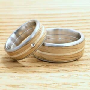 Zwei Ringe auf einer Holzoberfläche verkörpern die Essenz einer Hochzeit. Sie verfügen über Holzeinlagen mit silbernen Rändern, perfekt für diejenigen, die ihren Traumtag planen. Ein Ring ist elegant mit einem kleinen Diamantakzent verziert.