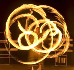 Inmitten der faszinierenden Darbietung dreht eine Person mehrere brennende Poi in komplizierten Schleifen und erzeugt so helle Feuerspuren vor einem dunklen Hochzeitshimmel. Die feurigen Muster bilden wirbelnde, fließende Formen und fangen die Bewegung und Energie ein, die die Leidenschaft einer frisch vermählten Feier widerspiegeln.