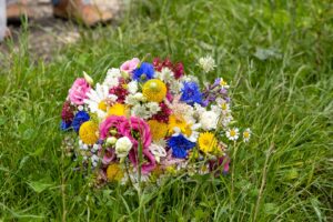 Ein lebendiger Strauß aus Gänseblümchen, Rosen und anderen bunten Blüten liegt auf einer üppigen grünen Wiese und schafft die perfekte Kulisse für Ihre Hochzeit. Die rosa, gelben, weißen und blauen Blumen bilden eine lebendige und malerische Szene, die sich ideal für die Hochzeitsplanung eignet.