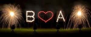Ein atemberaubendes Pyrotechnik-Display buchstabiert „B❤️A“ mit einem Herz in der Mitte, flankiert von leuchtenden Feuerwerken vor dem dunklen Himmel – eine magische Note für jede Hochzeitsfeier.