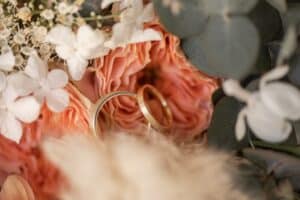 Zwei goldene Eheringe zwischen rosa Rosen, weißen Blumen und Eukalyptusblättern ergeben ein romantisches und elegantes Hochzeitsarrangement.