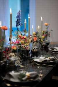 Ein elegant gedeckter Esstisch mit großen brennenden Kerzen, bunten Blumenarrangements und ordentlich gefalteten Servietten weckt den Charme einer Hochzeitsfeier. Gläser und Teller sind für mehrere Gäste arrangiert und schaffen eine anspruchsvolle und einladende Atmosphäre, die perfekt für unvergessliche Momente bei der Hochzeitsplanung ist.
