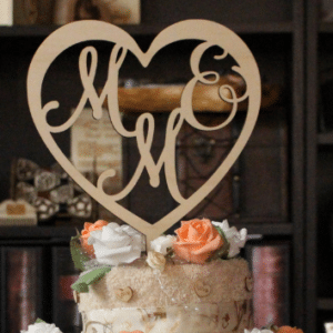 Im Mittelpunkt steht eine Torte, die mit einem hölzernen Herz mit der aufwendigen Inschrift „M & E“ geschmückt ist – perfekt für eine Hochzeitsfeier. Sie ist wunderschön mit orangefarbenen und weißen Rosen dekoriert und steht vor einem verschwommenen Hintergrund aus Büchern und Dekorationsgegenständen. Sie verkörpert die Essenz eleganter Hochzeitsplanung.