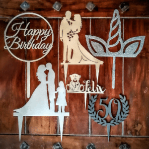 Verschiedene Tortenaufsätze auf einer Holzoberfläche, darunter ein „Happy Birthday“-Schild, eine Paarsilhouette perfekt für die Hochzeitsplanung, ein Einhornhorn mit Ohren, eine „50“ in einem Lorbeerkranz und der Name „Felix“ mit einer Hundesilhouette.