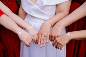 Vier Personen stehen nebeneinander mit ausgestreckten Armen und zeigen passende Armbänder. Sie tragen aufeinander abgestimmte rot-weiße Outfits, perfekt für eine stilvolle Hochzeitsfeier.