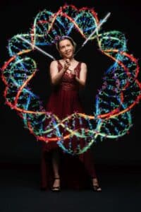 Eine Frau in einem weinroten Kleid lässt LED-Poi rotieren und erzeugt so vor dem dunklen Hintergrund ein buntes Muster, das an DNA-Helices erinnert und der Hochzeitsfeier ein faszinierendes Flair verleiht.