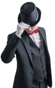 Eine Person in einem schwarzen Anzug mit roter Fliege, bereit für die Hochzeit, lüftet einen schwarzen Zylinder und trägt weiße Handschuhe. Der Hintergrund ist schlicht weiß.