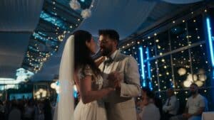 Braut und Bräutigam tanzen bei ihrem Hochzeitsempfang. Die Braut trägt ein weißes Kleid mit Schleier, während der Bräutigam einen hellen Anzug trägt. Der Veranstaltungsort ist mit Lichterketten und weißen Vorhängen dekoriert und schafft eine romantische Atmosphäre, die perfekt ist, um ihre Liebe und Heirat zu feiern.