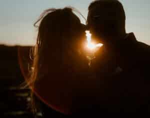 Die Silhouette eines Paares teilt einen intimen Moment bei Sonnenuntergang, wobei die Sonne ihre Profile beleuchtet und einen warmen Schein um sie herum erzeugt – eine perfekte Szene, die an eine romantische Hochzeit erinnert.