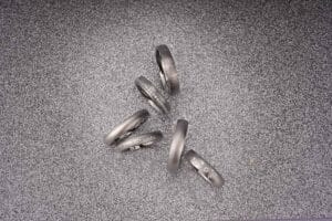 Fünf silberne Ringe mit kleinen eingelassenen Steinen sind diagonal auf einer strukturierten grauen Oberfläche angeordnet und fangen die Essenz zeitloser Eleganz ein, perfekt für jede Hochzeitsplanung.