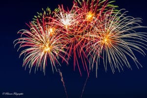 Ein farbenfrohes Feuerwerk erhellt den Nachthimmel mit roten, gelben und grünen Streifen und schafft eine festliche und feierliche Atmosphäre – und fängt die Freude und Romantik einer Hochzeit vor einem dunklen Hintergrund perfekt ein.
