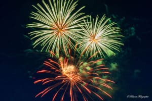 Ein schillerndes Feuerwerk erleuchtet den Nachthimmel, perfekt für eine Hochzeitsfeier. Helle grüne und rote Feuerwerke schaffen vor dem dunklen Hintergrund eine lebendige und festliche Atmosphäre und fangen die Aufregung und Schönheit ein, die an fröhliche Hochzeitsfeierlichkeiten erinnert.