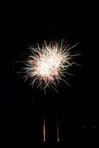 Ein helles, farbenfrohes Feuerwerk erhellt den Nachthimmel mit roten, weißen und glitzernden Flammen. Perfekt für eine Hochzeitsfeier, das leuchtende Feuerwerk schafft vor dem dunklen Hintergrund eine festliche Atmosphäre und verleiht dem besonderen Tag eines jeden Paares Magie.