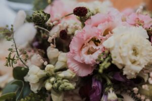 Eine Nahaufnahme eines Blumenarrangements mit rosa Lisianthus, weißen Rosen und verschiedenen kleinen Knospen und Blättern. Die sanften Farben und zarten Blütenblätter sorgen für ein üppiges, romantisches Gefühl.