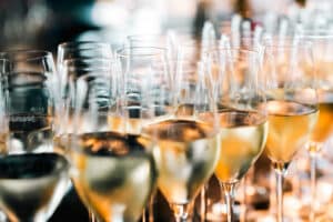 Dicht an dicht stehen Reihen von mit Sekt gefüllten Champagnerflöten, die warmes Licht einfangen, Reflexe erzeugen und so eine festliche, feierliche Atmosphäre schaffen.