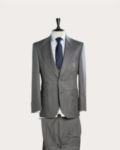 Eine Schaufensterpuppe präsentiert einen grauen Anzug mit dazu passender Jacke und Hose. Die Jacke ist zugeknöpft und wird über einem weißen Hemd getragen, dazu eine dunkle Krawatte mit Tupfenmuster. Der Hintergrund ist schlicht weiß.