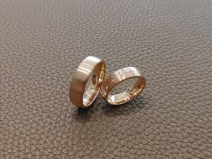 Zwei goldene Ringe ruhen auf einer braunen, strukturierten Oberfläche. Ein Ring ist schlicht und poliert, während der andere gravierte Motive und kleine eingelassene Steine aufweist.