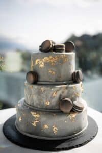 Eine dreistöckige Torte aus grauem Marmor, verziert mit Blattgold und gekrönt mit Schokoladenmacarons, auf einer schwarzen Schiefertafel.